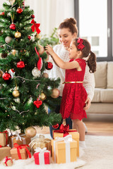 family, winter holidays and people concept - happy mother and little daughter decorating christmas t