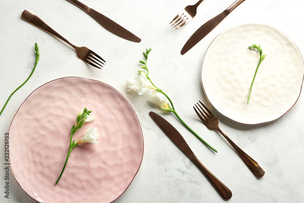 Plates with cutlery and flowers on light background