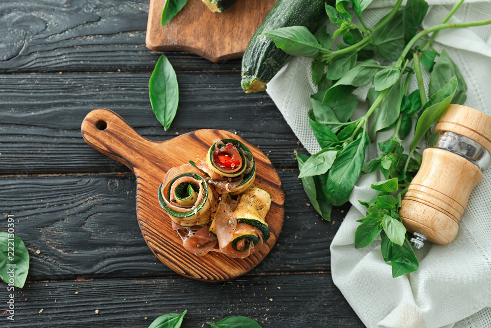Tasty zucchini rolls with prosciutto on wooden board