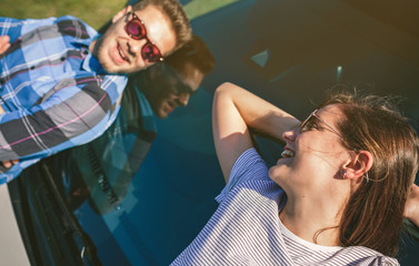 Happy young couple resting lying on the windshield of the car