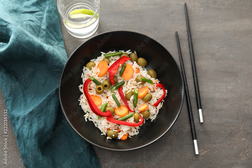 Bowl with tasty boiled rice and vegetables on grey table