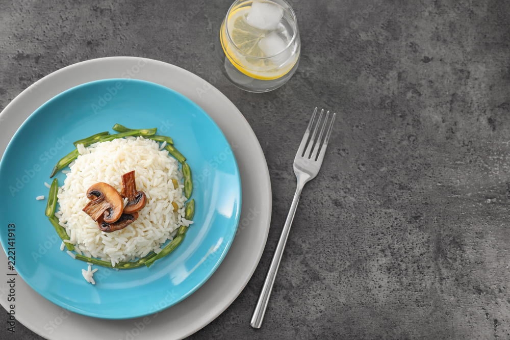 Plate with tasty boiled rice, mushrooms and green beans on grey table