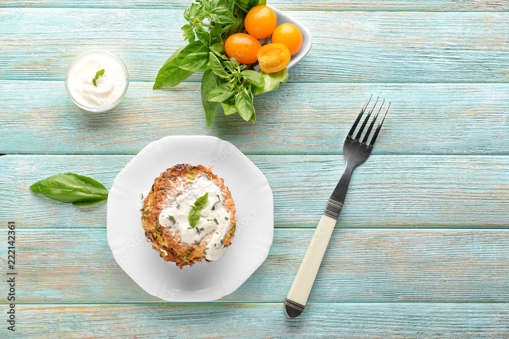 Plate with zucchini pancakes and sauce on wooden table