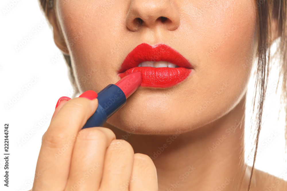 Beautiful young woman applying red lipstick on white background, closeup