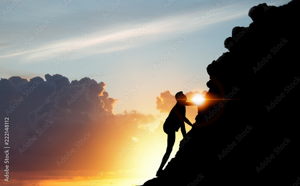 A silhouette of man climbing on mountain top over sunset background ...