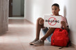 © Pixel-Shot - African-American teenage boy holding sheet of paper with word BULLYING while sitting on floor at school