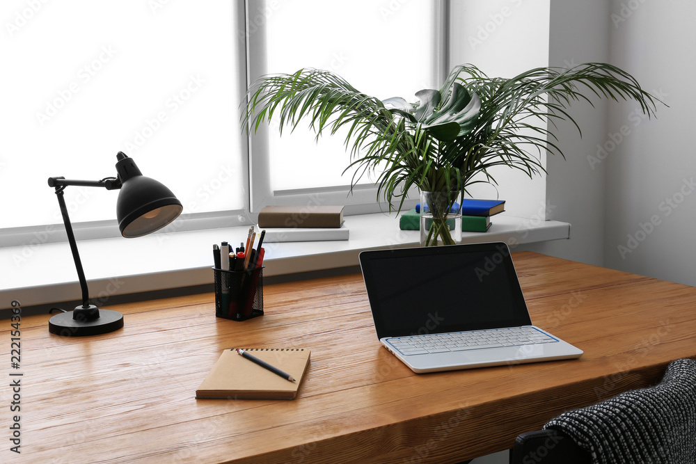Workplace with laptop and tropical leaves in vase on table