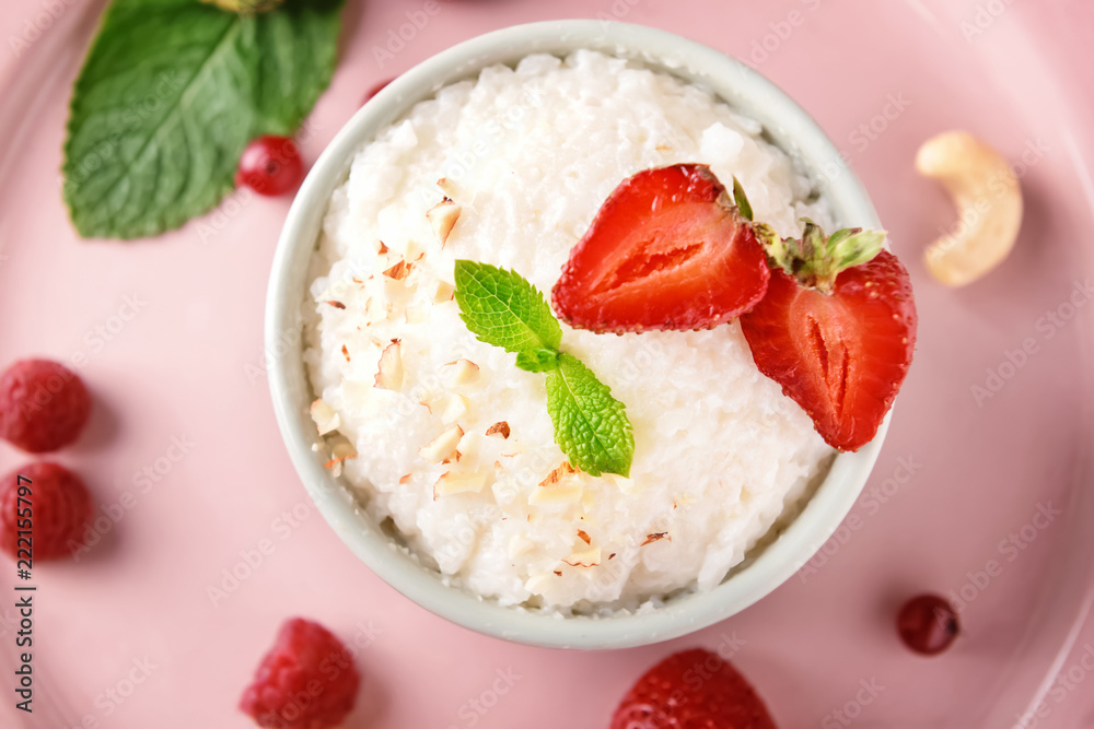 Delicious rice pudding with berries in bowl on color plate, closeup