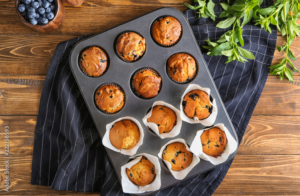 Baking tin with blueberry muffins on wooden table