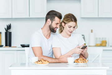 Wall Mural - beautiful happy young couple using smartphone while having breakfast together