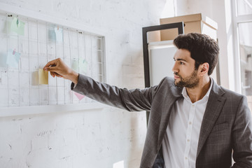 Wall Mural - handsome businessman putting paper sticker on task board in office