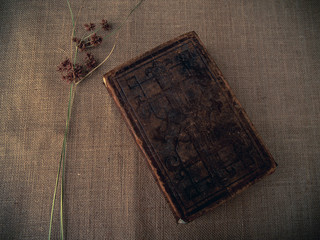 Vintage style. closed antique book with dry grass and red thread with burlap background