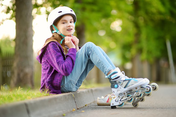 Wall Mural - Pretty little girl learning to roller skate on summer day in a park. Child wearing safety helmet enjoying roller skating ride outdoors.