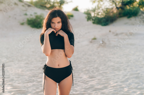 A sexy girl in a separate trendy swimsuit is standing on the beach, is  removed for a fashion magazine, posing as a wild cat on the sand. Stock  Photo | Adobe Stock