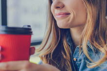 Concept Of Calmness And Relaxation. Smiling Woman Holding A Cup Is Going To Drink Coffee. She Is Sitting In A Cafe Near The Window. Close Up, Cropped Photo