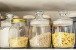 on a white kitchen shelf glass jars with groats, macaroni, cornflakes