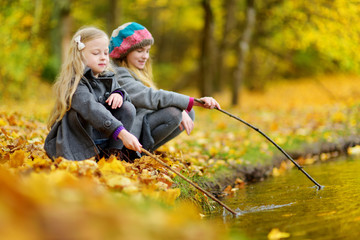 Cute little girls playing by the water on beautiful autumn day. Happy children having fun in autumn park.