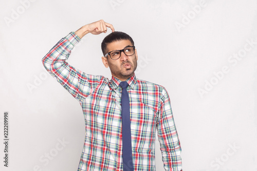 Fotografía portrait of thoughtful handsome bearded businessman in colorful checkered shirt, blue tie and eyeglasses standing and looking away with funny face