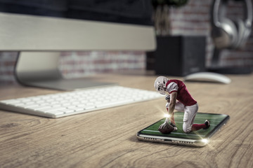 Wall Mural - Football Player with a red uniform playing and coming out of a full screen phone on a wooden table.