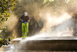 Fototapeta Tęcza - utility service company sweeper worker cleaning public park with water pressure in city