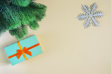 On A Beige Background A Gift In A Turquoise Box With An Orange Bow, A Snowflake And A Spruce Branch. A Place For Inscriptions And Texts, Mock Up.
