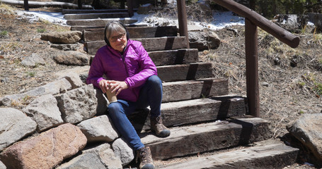 Wall Mural - Happy elderly woman seated on stairs smiling at camera in forest