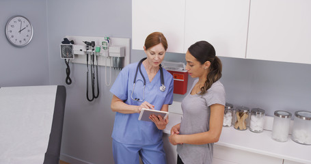 Wall Mural - Portrait of beautiful latina patient looking at test results on tablet with middle aged nurse. Close view of attractive female hispanic patient looking at health condition on tablet device with nurse