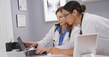Portrait Of Two Medical Physicians Looking At Lab Results Of Patient On Laptop Computer. Close Up Of Senior Medical Doctor Discussing Ct Scans On Computer With Young Colleague