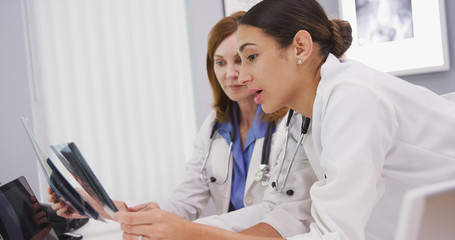 Young medical colleague discussing x rays of patient with senior doctor in her office. Two medical physicians reviewing xrays of patient hands and wrists indoors hospital clinic