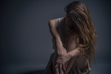 Depressed young woman sitting in a dark corner, crushed and alone