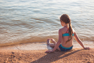 blonde cute seven year old girl sitting on the beach during vacation