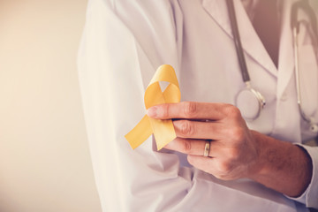 doctor hands holding yellow gold ribbon, sarcoma awareness, childhood cancer awareness