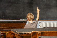 Concept Of Public Primary School Education With Young Boy Raising His Hand In The Classroom