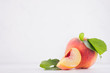 © finepoints - Ripe peach with green leaves, pulpy slice on white light wooden table, copy space.