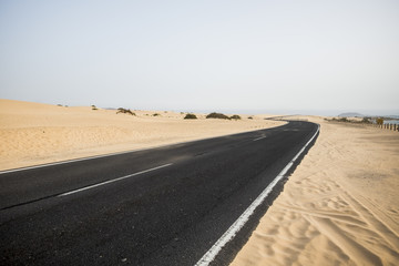 black asphalt road in the middle of the desert crossing the dunes of sand in fuerteventura corralejo natural park area. feel of adventure with nobody there. alternative place for tourism or vacation