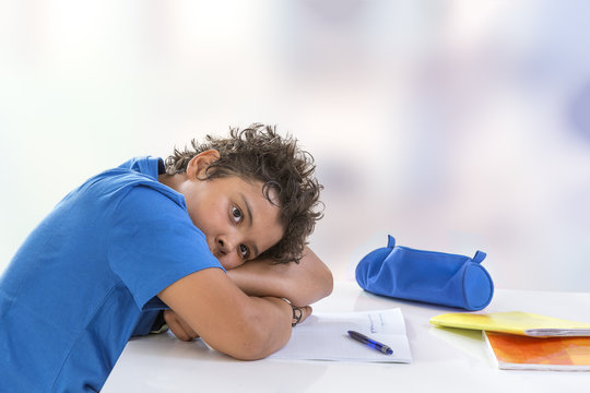 Overwhelmed schoolboy. Bored and tired teenage boy doing homework on desk in his room,seems sleepinp