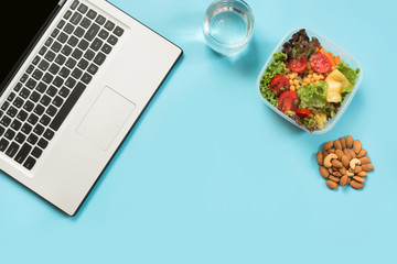 healthy business lunch in office, salad, almonds, water on blue. top view with copy space. concept h