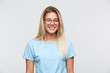 Portrait of smiling beautiful young woman with blonde hair wears glasses and blue t shirt feels happy isolated over white background