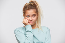 Portrait Of Unhappy Disappointed Young Woman With Blonde Hair And Ponytail Wears Blue Sweatshirt Looks Bored And Sad Isolated Over White Background