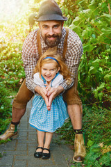 Wall Mural - Man  in traditional bavarian clothes Lederhose with little girl on his hands in dirnndl. Papa and daughter having fun outdoor