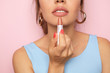 Beautiful young woman applying pink lipstick on color background, closeup