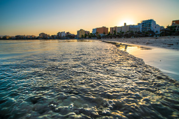 Poster - Golden waves of the sea and city on horizon during sunset