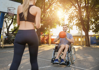 Poster - Young man in wheelchair and sporty woman training with ball outdoors