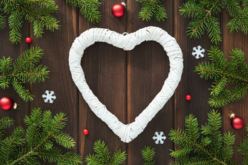 Wall Mural - Christmas card with place for your text. White heart made of branches with decorations of snowflakes, stars, red glass balls, beads and green fir branches against background of brown worn wooden board