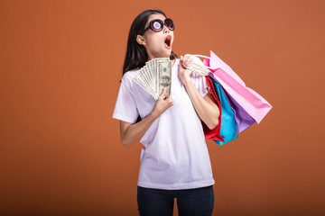 Woman holding shopping bag and cash isolated in orange background.