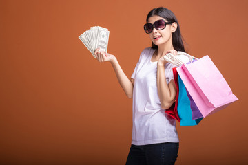 Woman holding shopping bag and cash isolated in orange background.