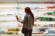 Pretty girl in eyeglasses and striped shirt choosing milk in dairy department in supermarket