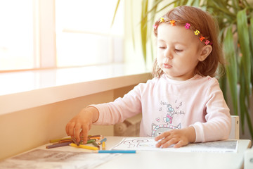 Little girl draws sitting at table