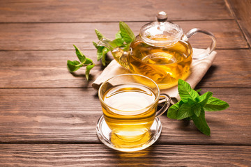 Tea in a transparent cup and teapot from fresh melissa leaves on a wooden background.