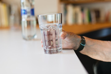 Wall Mural - Hand of senior lady holding a glass of water on table